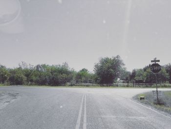 Empty road by trees against sky