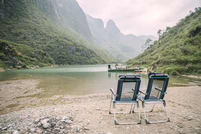 Chair and table by lake against mountains