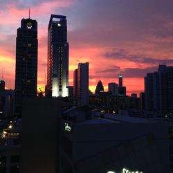 Illuminated cityscape against cloudy sky at dusk