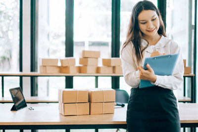 Smiling young woman holding camera while standing in box