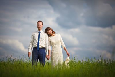 Couple holding hands while standing on grassy field against sky