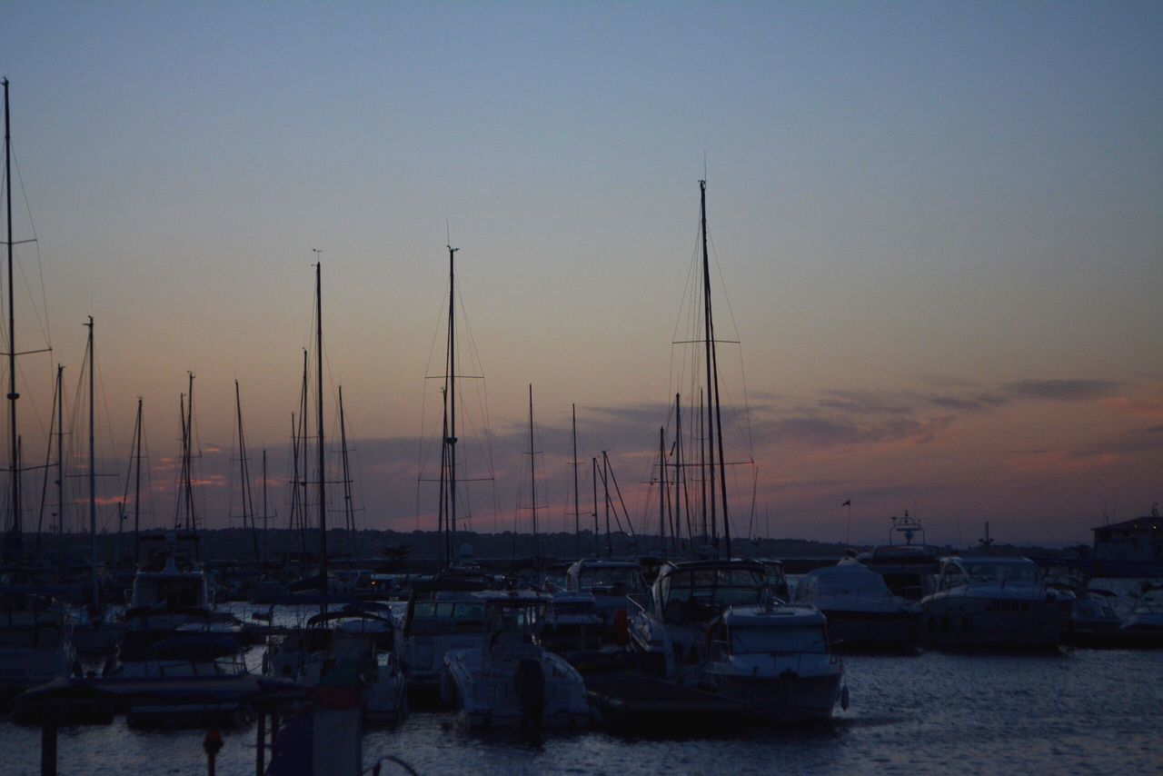 nautical vessel, transportation, moored, mast, mode of transport, harbor, boat, sea, sunset, sailboat, water, ocean, tranquility, sky, calm, in a row, abundance, nature, tranquil scene, in front of, no people, waterfront, large group of objects, dramatic sky, non-urban scene, marina, scenics