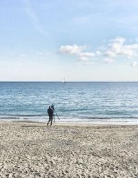 Rear view of man with camera on beach against sky