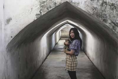 Portrait of young woman holding cat standing against wall