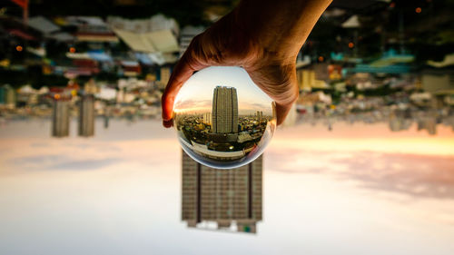 Close-up of hand holding cityscape against sky