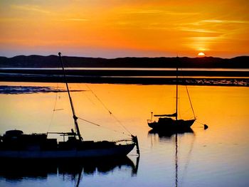 Silhouette sailboats on lake against orange sky