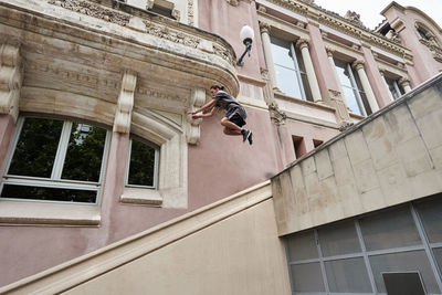 Focused young male jumping over stone steps in city while doing parkour and showing trick