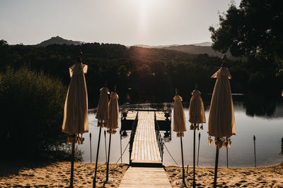 Wooden poles hanging by trees in lake against sky