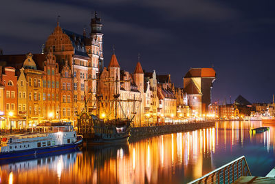 Illuminated buildings by river against sky at night