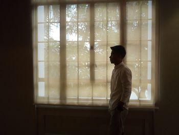 Side view of man standing against window
