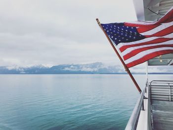American flag on railing by sea against sky