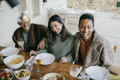 Cheerful woman sitting with men sitting at dining table in patio enjoying dinner party