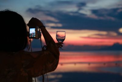 Rear view of silhouette man photographing sea against sky during sunset