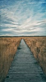 Boardwalk on field against sky