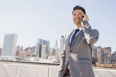 Portrait of a young businessman talking on his smartphone on a rooftop overlooking the city