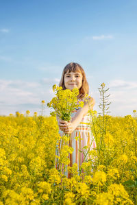 Portrait of woman standing amidst yellow flowering plants on field against sky