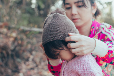 Close-up of mother putting knit hat for baby girl while sitting outdoors