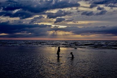 Silhouette people on beach against sky during sunset