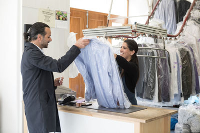 Smiling mature female owner giving shirts to male customer while standing at checkout