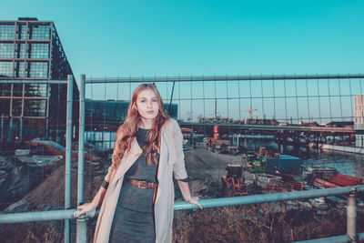 Portrait of young woman standing by railing against sky