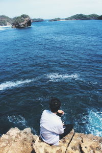 Rear view of man sitting on rock by sea