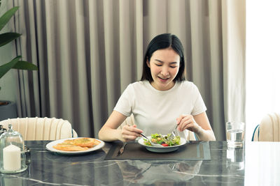 Young woman looking away while sitting on table