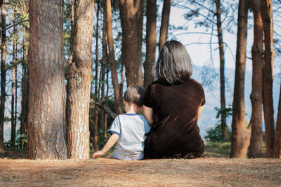 Rear view of mother with son sitting on field in forest