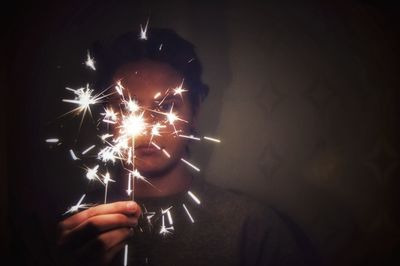 Close-up of teenage boy holding sparkler at night