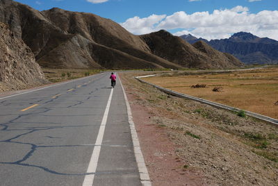 Man cycling on road by mountains against sky