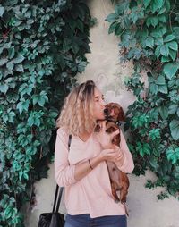 Young woman kissing dog while standing against wall in park