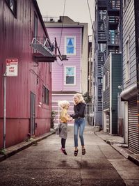 Full length of siblings jumping on footpath