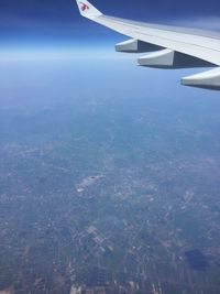 Aerial view of airplane wing over cityscape against blue sky