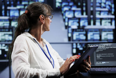 Side view of young woman using mobile phone while standing in office