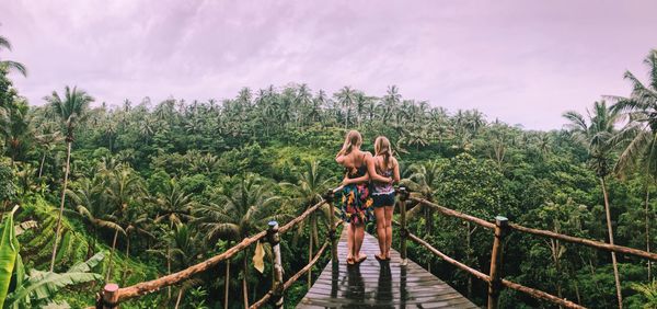 Panoramic view of friends on wet footbridge against sky