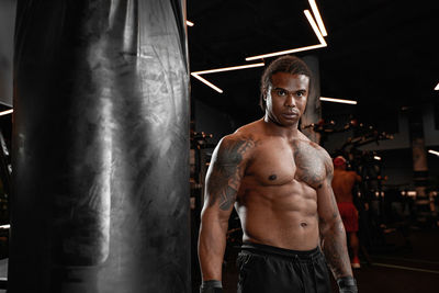 Portrait of shirtless man standing against black background