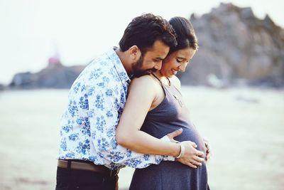 Smiling husband touching pregnant belly of wife at beach