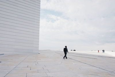 Man walking on walkway at oslo opera house against sky