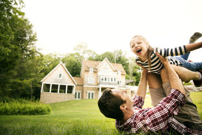 Playful man playing with daughter in backyard against sky