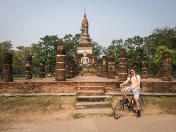 Young man riding bicycle in front of ruins of sukhothai historical park, thailand