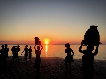 Silhouette people on beach against sky during sunset