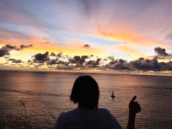 The women back with thumbs up on sunset in the ocean silhouette