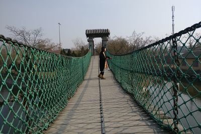 Side view of woman standing on footbridge over river in city