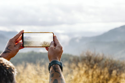 Cropped hands photographing cloudy sky through smart phone during summer