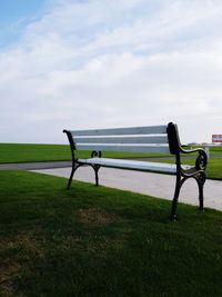 Empty bench on field against sky