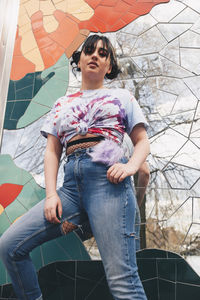 Low angle portrait of young woman standing against mosaic wall