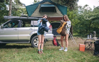 Friends with backpacks standing on grassy field at campsite in forest
