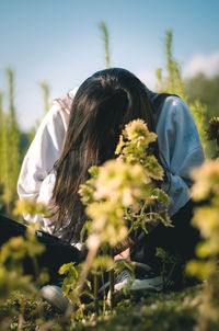 Midsection of woman midst flowering plants on field against sky