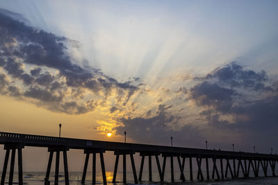 Silhouette bridge over sea against sky during sunset