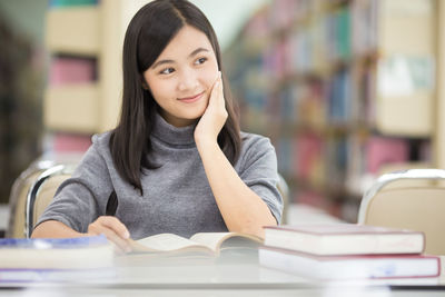 Young woman reading book while sitting at table in library