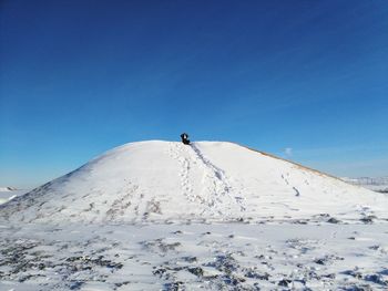 Distant view of girl sitting on ski slope against blue sky